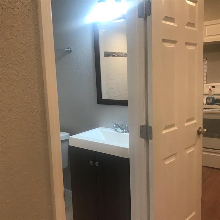 A small bathroom with a dark vanity, white sink, and mirror, viewed through a doorway — 1000 10TH AVENUE NW UNIT 3, LARGO, FL