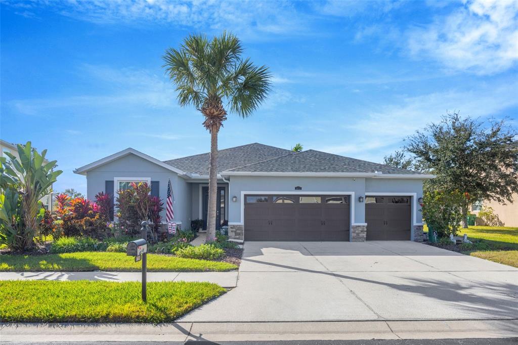 A single-story house with a three-car garage, a palm tree, and a landscaped front yard — 5652 FISHER GLEN LOOP, WESLEY CHAPEL, FL