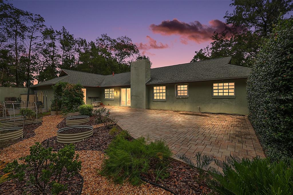 A single-story house with a paved patio, garden beds, and a chimney at dusk — 5040 SE 18TH STREET, OCALA, FL