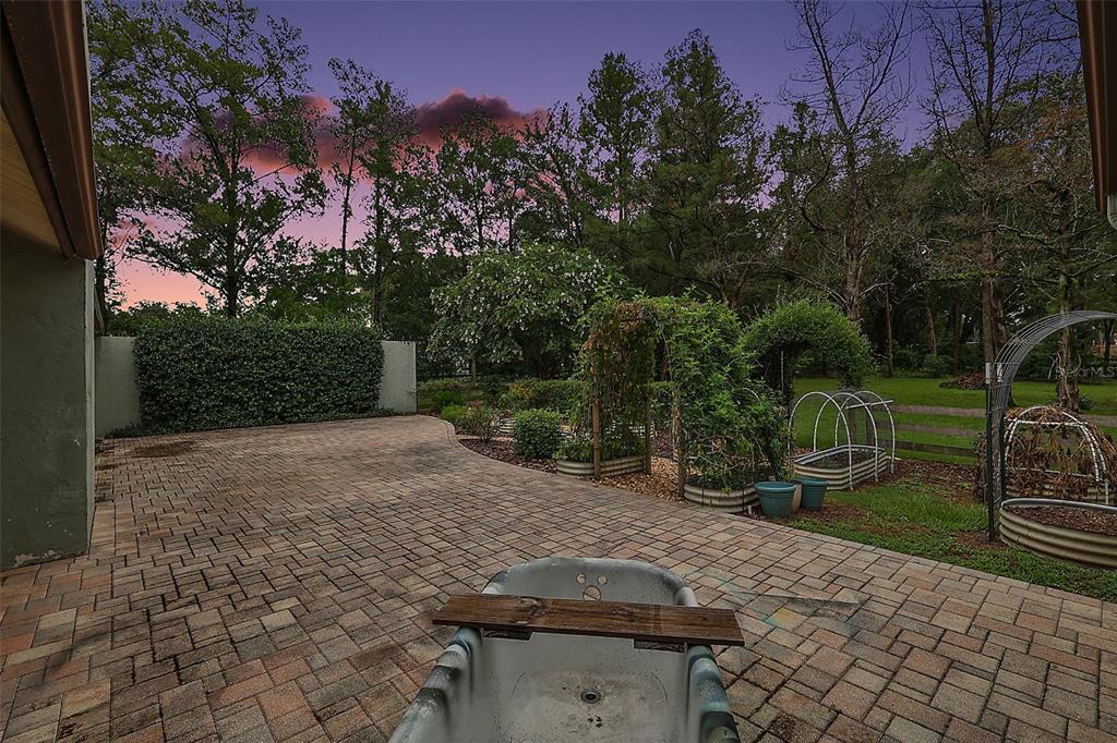 A stone patio features a vintage clawfoot bathtub and garden trellises at sunset — 5040 SE 18TH STREET, OCALA, FL