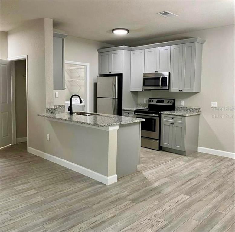 A kitchen with gray cabinets, stainless steel appliances, granite countertops, and wood-look flooring — 3011 HEMINGWAY CIRCLE UNIT 3011, HAINES CITY, FL