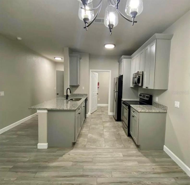 A kitchen features grey cabinets, granite countertops, stainless steel appliances, and wood-look flooring — 3011 HEMINGWAY CIRCLE UNIT 3011, HAINES CITY, FL