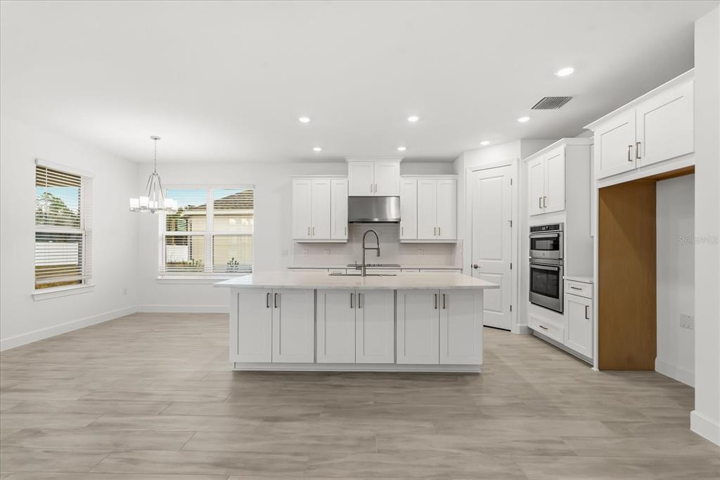 A bright, modern kitchen features white cabinetry, a large center island, and wood-look tile flooring — 4240 BARBUDA LANE, KISSIMMEE, FL