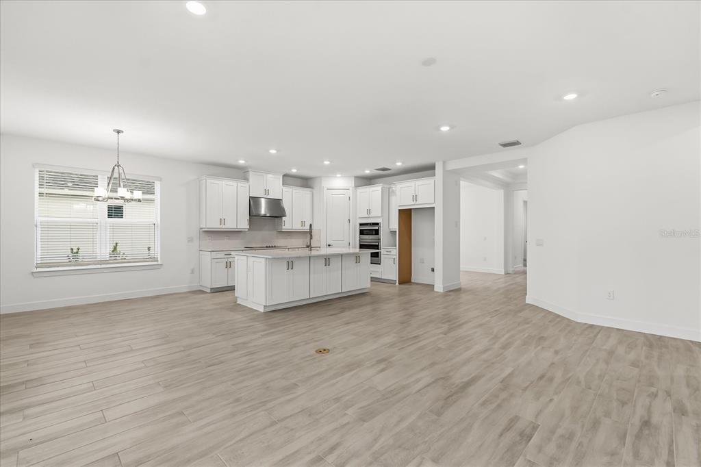A bright, open-concept kitchen features white cabinetry, a central island, and light wood-look flooring — 4240 BARBUDA LANE, KISSIMMEE, FL