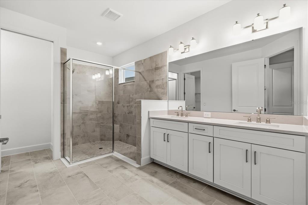 A bathroom features a double vanity with white cabinets, a large mirror, and a tiled shower — 4240 BARBUDA LANE, KISSIMMEE, FL