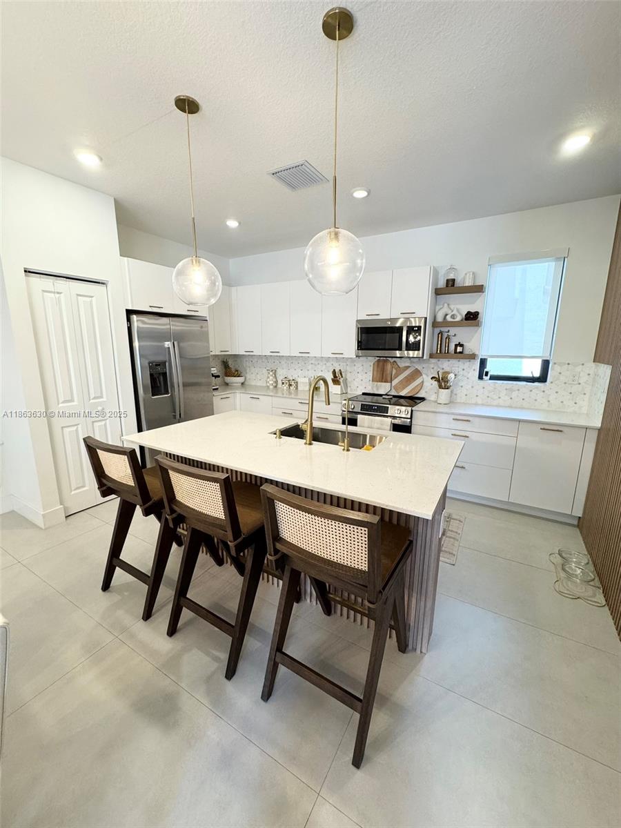 A modern kitchen features white cabinetry, a central island with bar seating, and pendant lighting — 4867 NW 84th Ave, Doral FL 33166, DORAL, FL