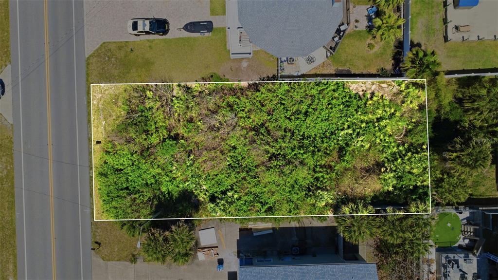 An aerial view shows a rectangular, undeveloped lot covered in dense vegetation between two houses — 6355 TURTLEMOUND ROAD, NEW SMYRNA BEACH, FL