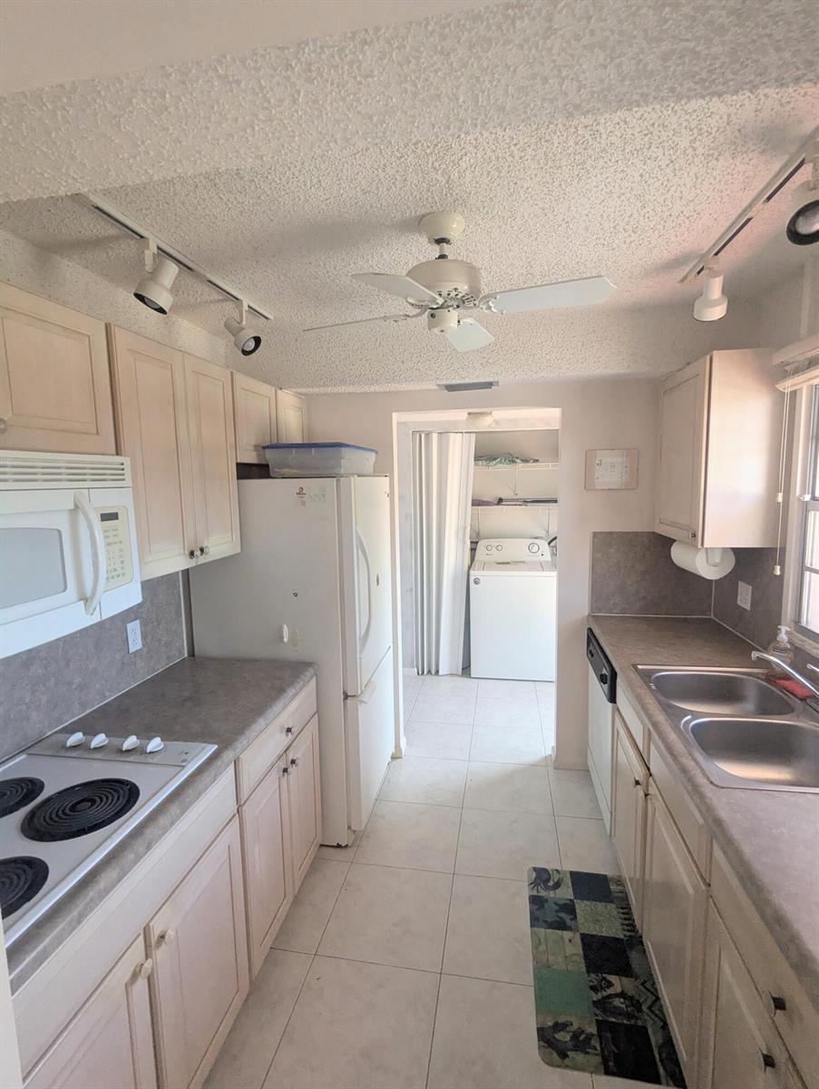 A galley kitchen features white cabinets, laminate countertops, a ceiling fan, and an adjacent laundry area — 2 Golfs Edge # D, West Palm Beach FL 33417, WEST PALM BEACH, FL