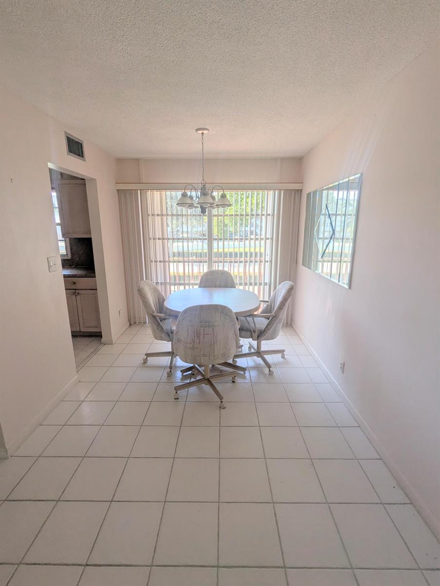 A dining area features a round table with four chairs, tile flooring, and a sliding door — 2 Golfs Edge # D, West Palm Beach FL 33417, WEST PALM BEACH, FL