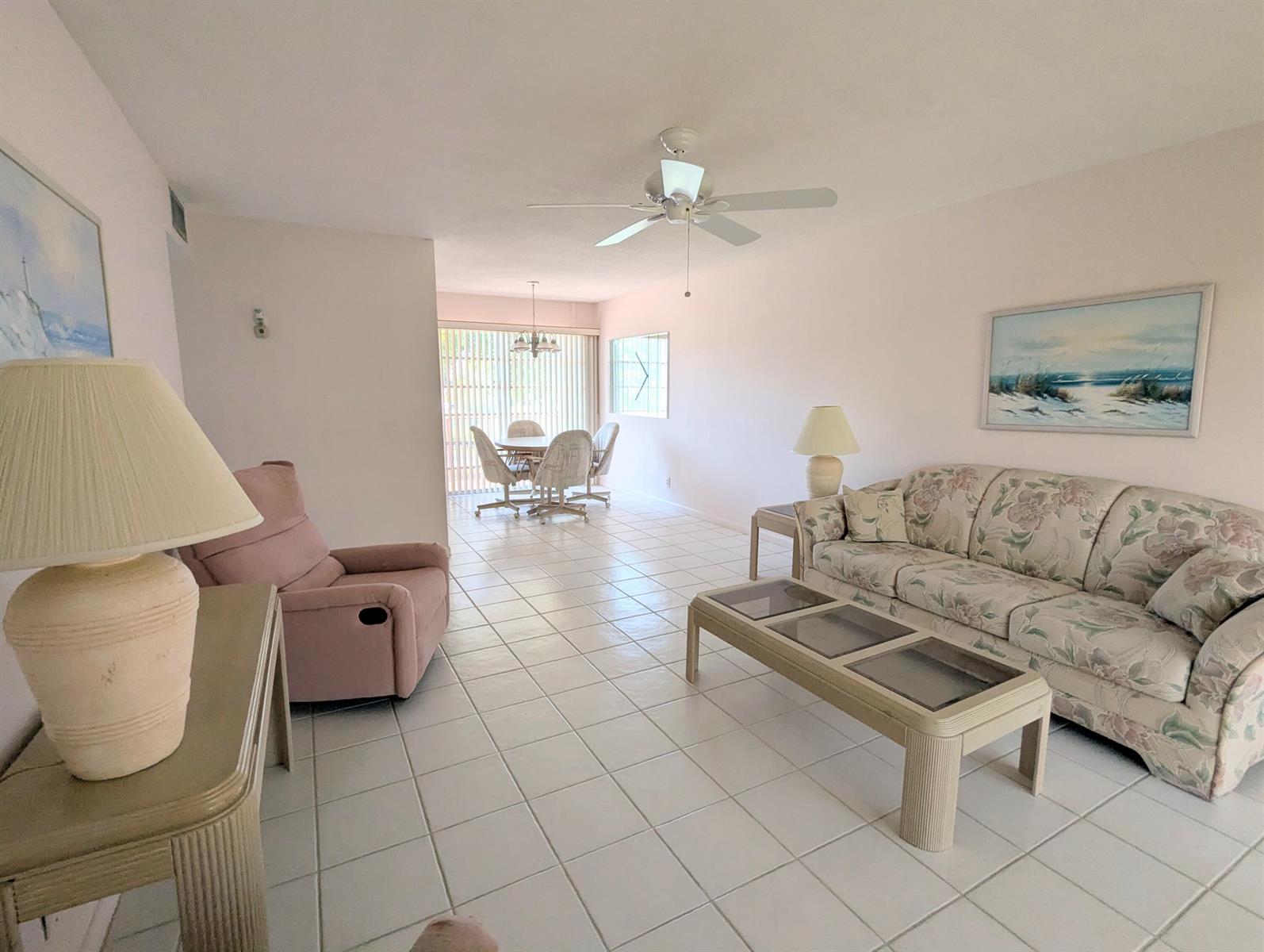 A living room with tile flooring, a floral sofa, a pink recliner, and a dining area — 2 Golfs Edge # D, West Palm Beach FL 33417, WEST PALM BEACH, FL