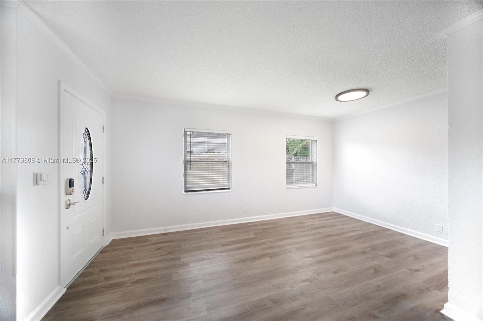 An empty room features white walls, wood-look flooring, two windows, and a white front door — 621 Hudson Rd, West Palm Beach FL 33405, WEST PALM BEACH, FL