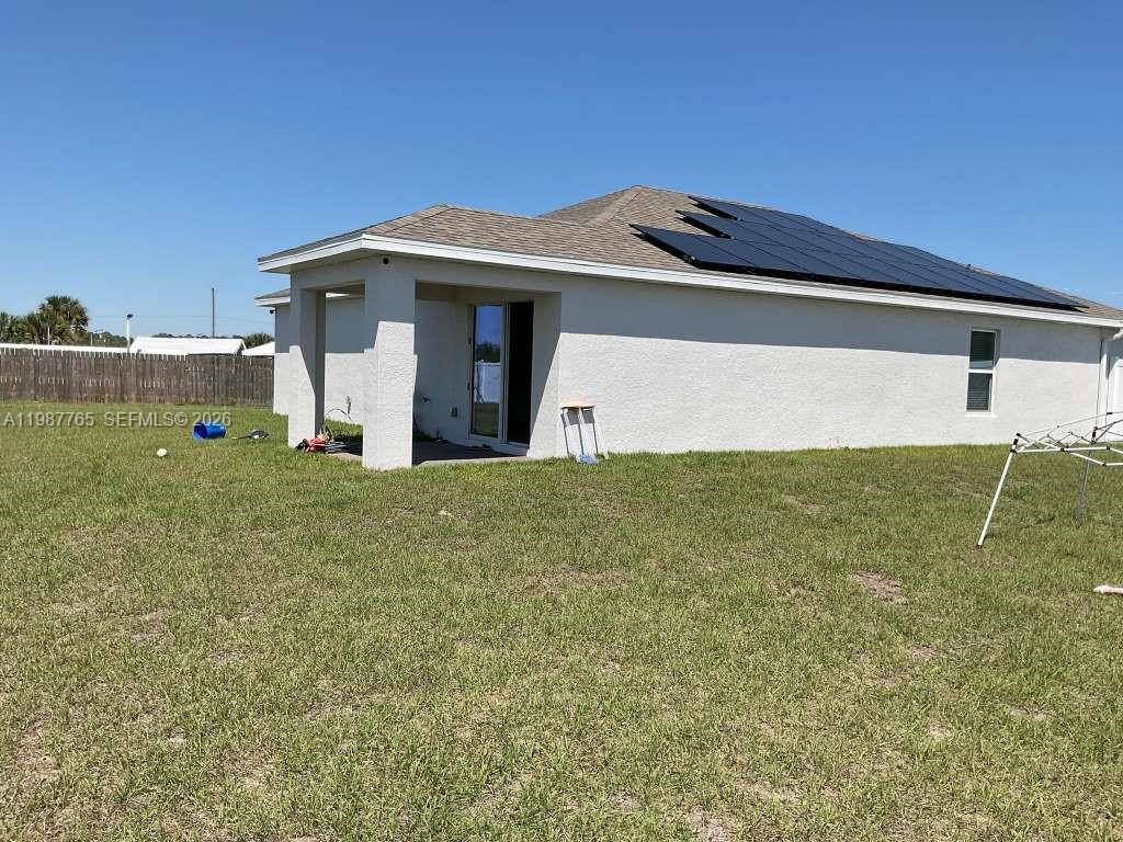 The exterior of a single-story house features a covered patio and rooftop solar panels — 9013 Meadow Cir, La Belle FL 33935, LA BELLE, FL