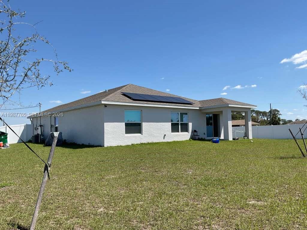 The rear exterior of a single-story house features a lawn, solar panels, and a patio — 9013 Meadow Cir, La Belle FL 33935, LA BELLE, FL