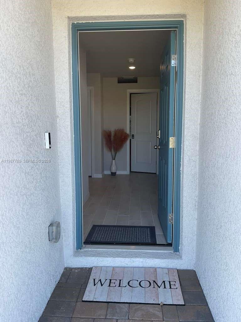 An open front door reveals a tiled entryway with a white door and decorative vase — 9013 Meadow Cir, La Belle FL 33935, LA BELLE, FL