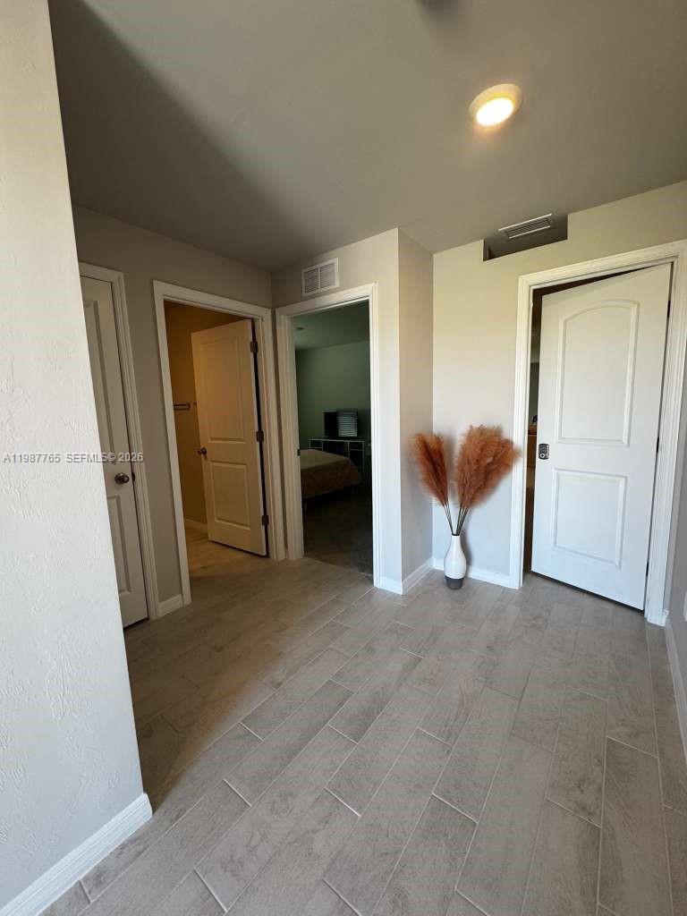 A hallway with light-colored tile flooring leads to two open doorways and a closed door — 9013 Meadow Cir, La Belle FL 33935, LA BELLE, FL