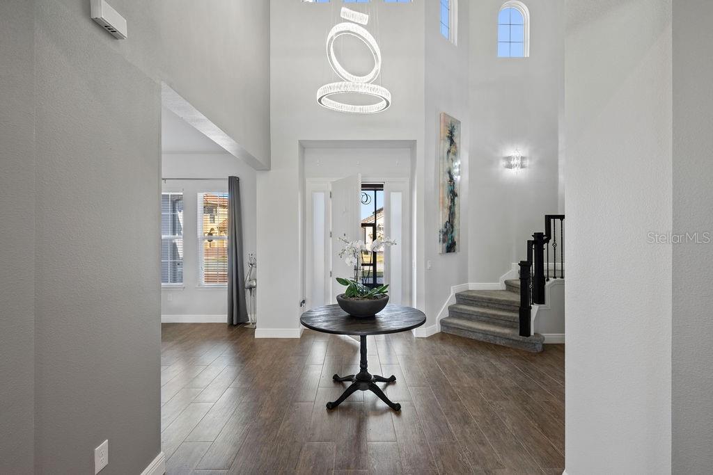 A bright foyer features a high ceiling, a modern chandelier, and a dark wood table — 840 SPINNAKER WAY, KISSIMMEE, FL