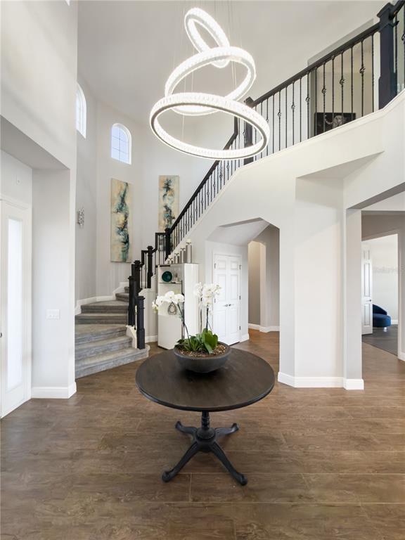 A foyer features a round wooden table, a modern chandelier, and a curved staircase — 840 SPINNAKER WAY, KISSIMMEE, FL