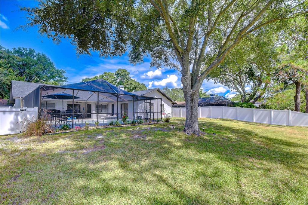 A backyard view of a house with a screened-in pool enclosure and a white fence — 16605 E COURSE DRIVE, TAMPA, FL