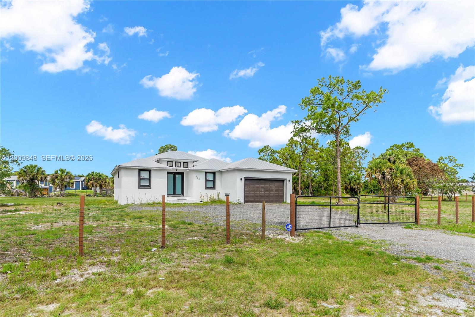 A single-story white house with a brown garage door sits behind a metal fence — 660 zambria, Clewiston FL 33440, CLEWISTON, FL