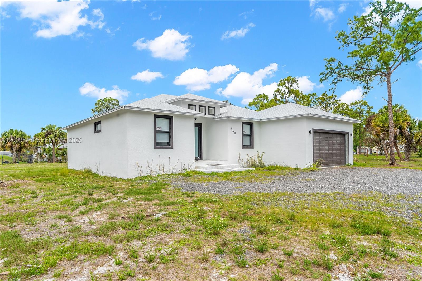 A white, single-story house with a gravel driveway and a dark-colored garage door — 660 zambria, Clewiston FL 33440, CLEWISTON, FL
