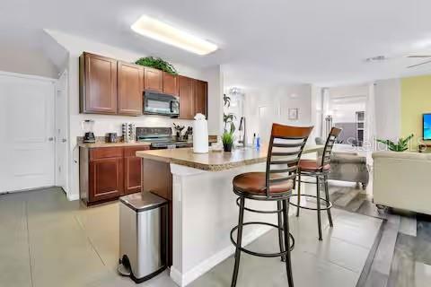 A kitchen with wooden cabinets, a breakfast bar with two stools, and stainless steel appliances — 10108 HAWK STORM AVENUE, TAMPA, FL