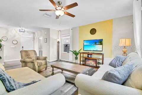 A living room features a ceiling fan, a patterned armchair, a sofa, and a television — 10108 HAWK STORM AVENUE, TAMPA, FL