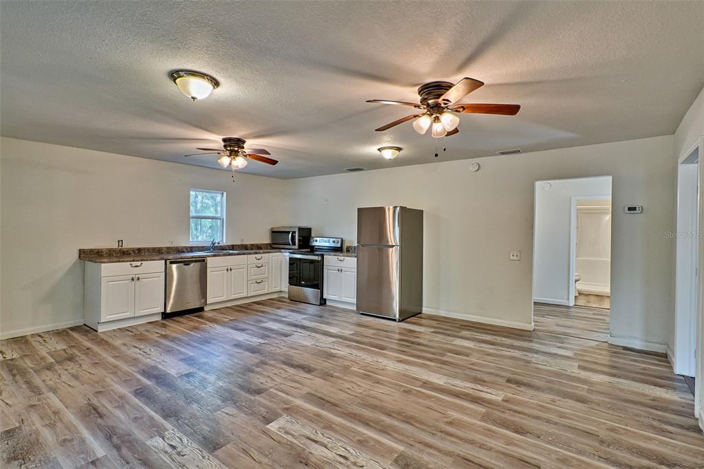 A kitchen features white cabinets, stainless steel appliances, and wood-look flooring in an open space — 300 S US HIGHWAY 129, BELL, FL