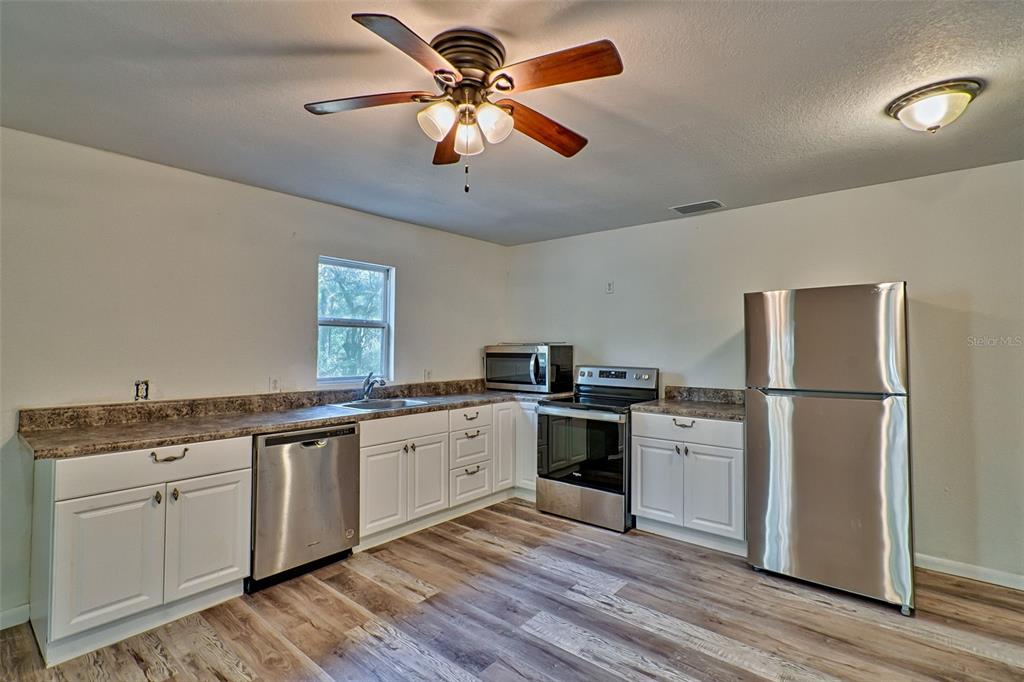 A kitchen features white cabinets, stainless steel appliances, laminate countertops, and wood-look flooring — 300 S US HIGHWAY 129, BELL, FL