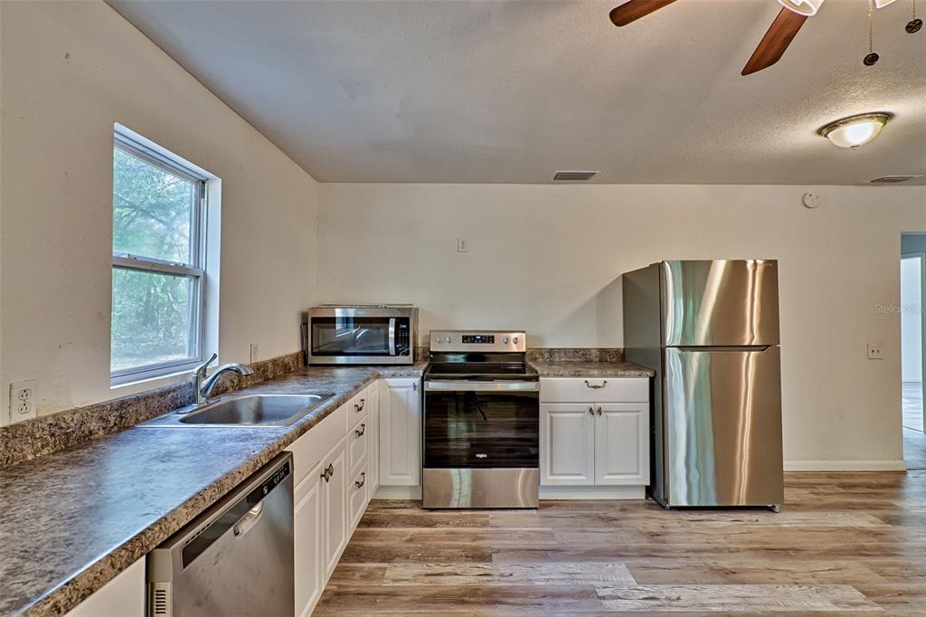 A kitchen features white cabinets, stainless steel appliances, a sink, and wood-look flooring — 300 S US HIGHWAY 129, BELL, FL