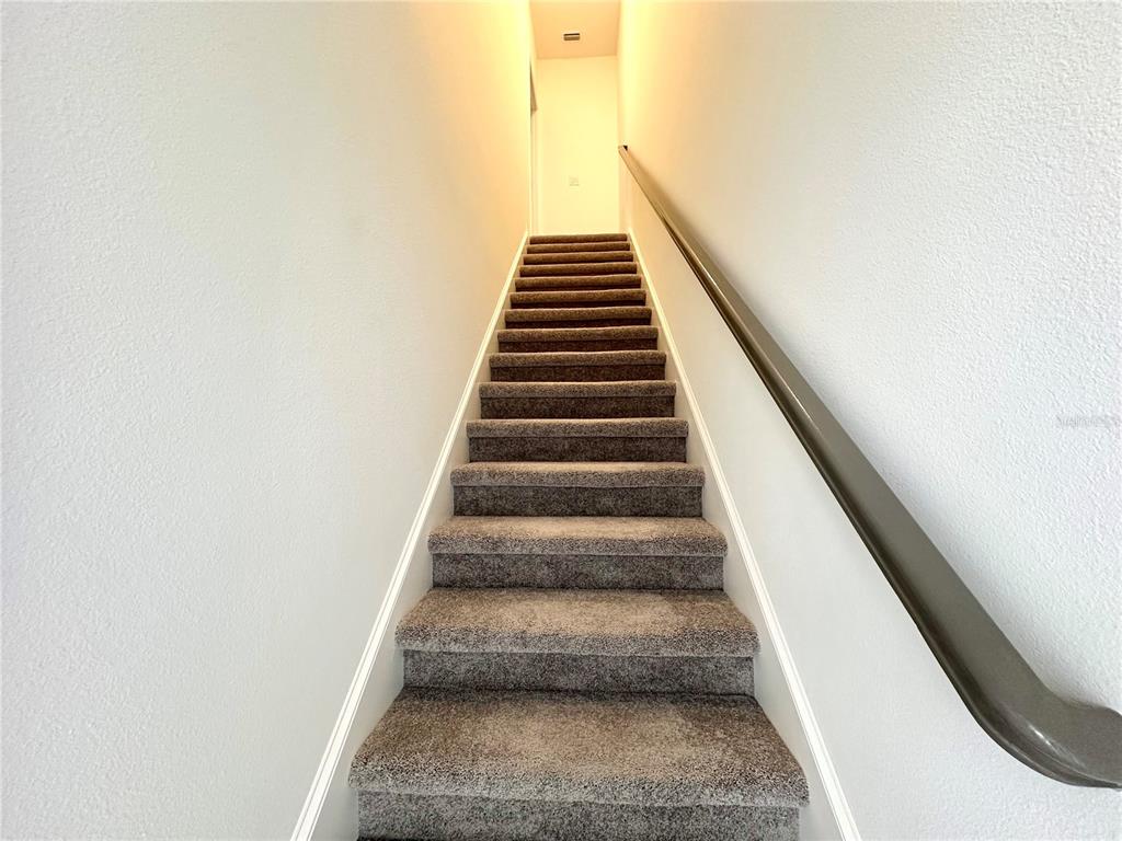 A straight staircase with gray carpeted steps and a dark handrail leads upward — 12761 HARVEST RAIN AVENUE, WINTER GARDEN, FL