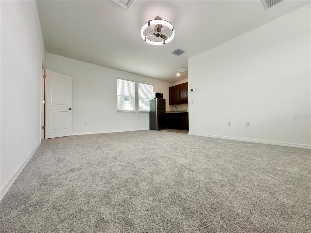 A carpeted room features a kitchenette with dark cabinets, a refrigerator, and a ceiling light — 12761 HARVEST RAIN AVENUE, WINTER GARDEN, FL