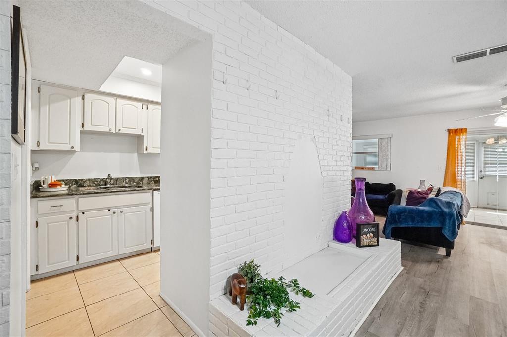 A white brick fireplace separates a tiled kitchen from a living room with wood flooring — 6232 GRETNA GREEN COURT N, PINELLAS PARK, FL