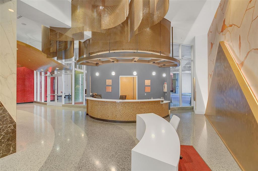 A modern lobby features a curved reception desk, a large metallic light fixture, and terrazzo flooring — 155 S COURT AVENUE UNIT 2705, ORLANDO, FL