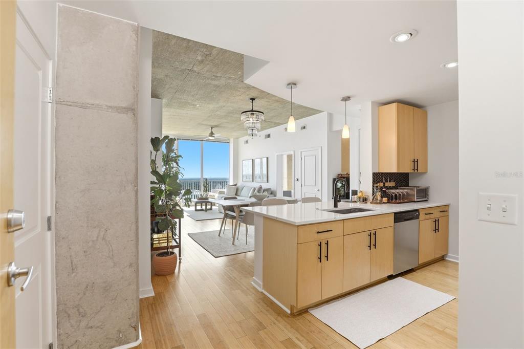A modern kitchen with light wood cabinets and a white island overlooks an open living area — 155 S COURT AVENUE UNIT 2705, ORLANDO, FL