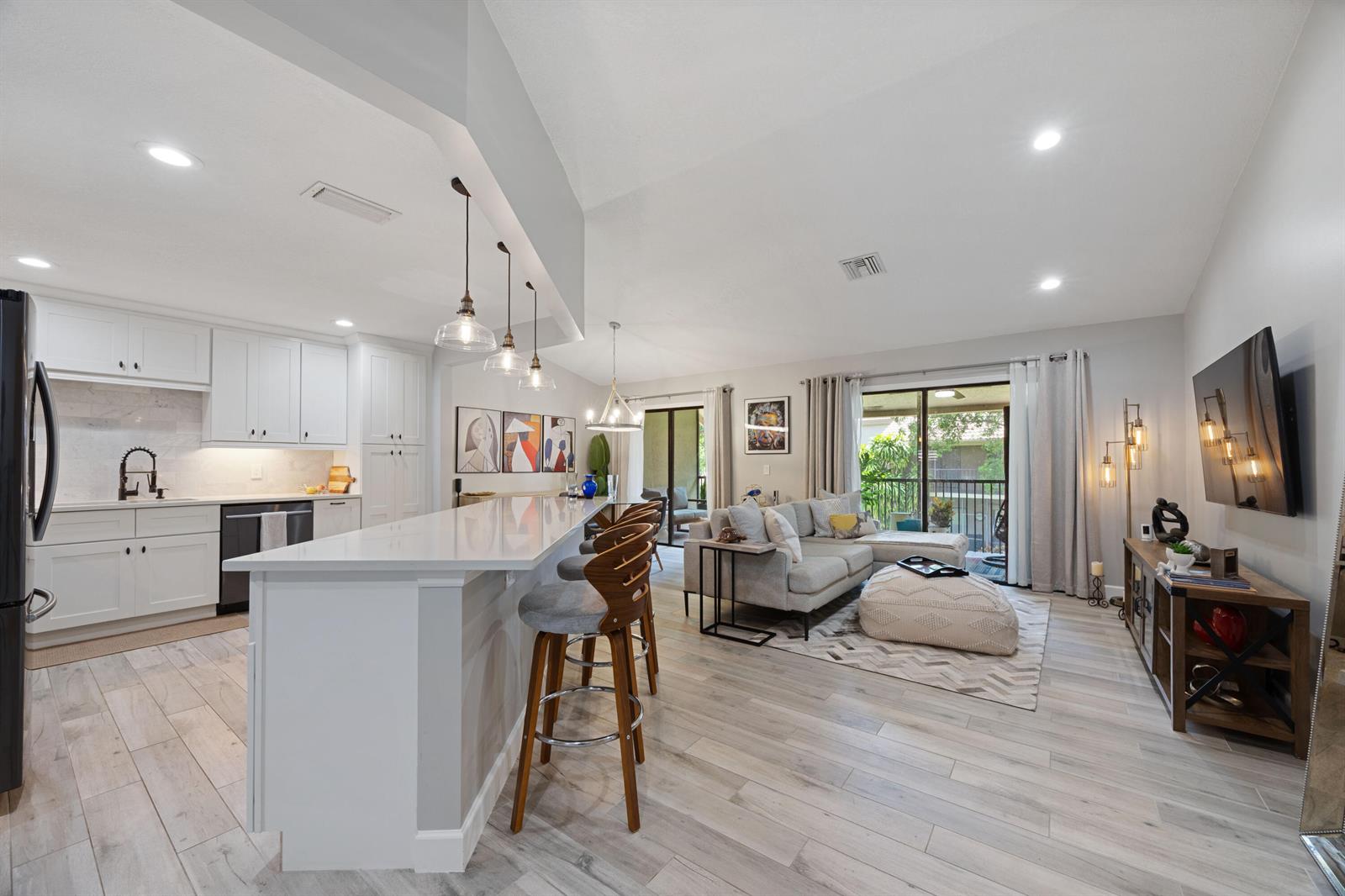 An open-concept kitchen and living area featuring white cabinetry, a breakfast bar, and wood flooring — 5710 Coach House Circle # F, Boca Raton FL 33486, BOCA RATON, FL