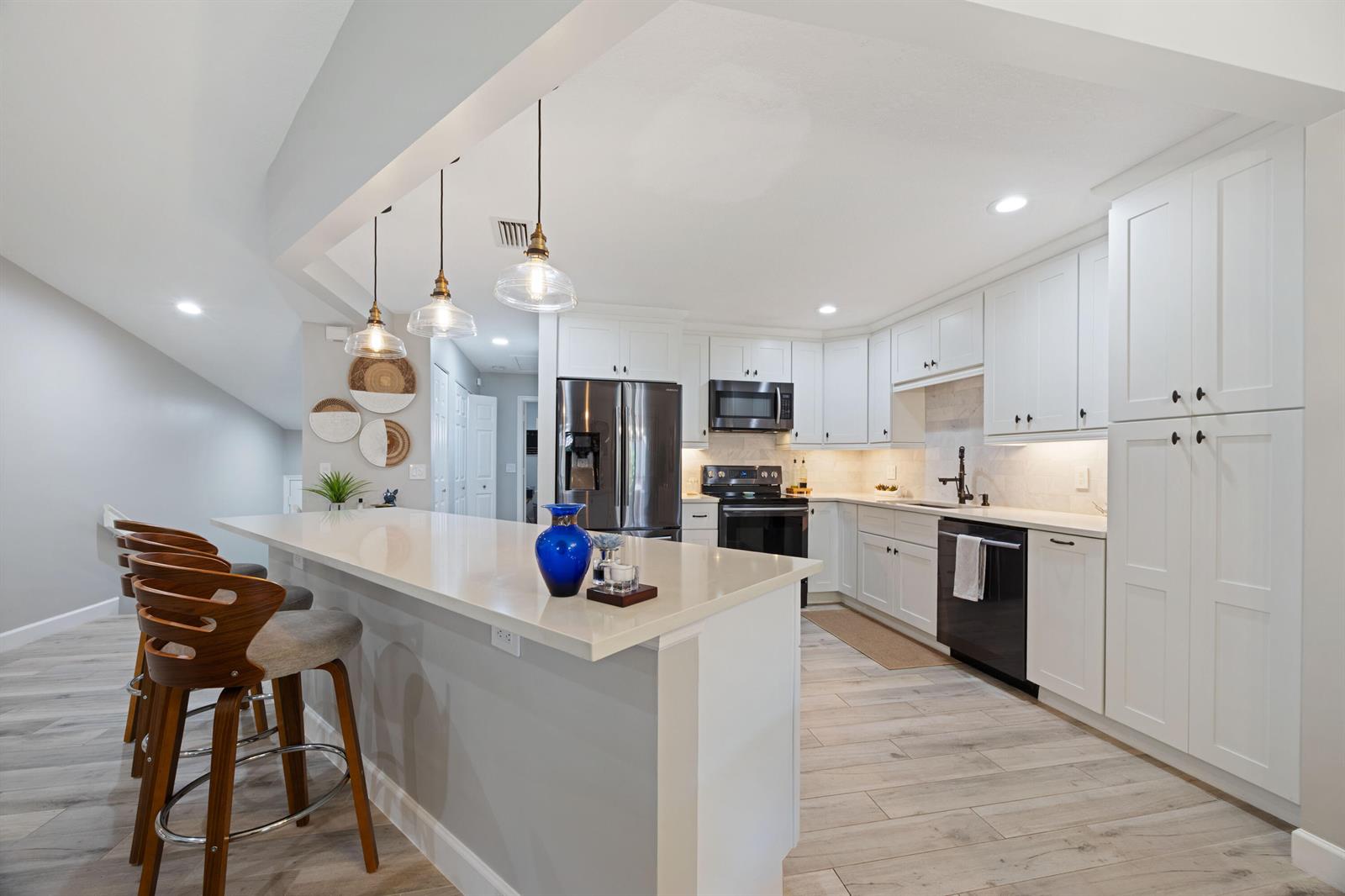 A modern kitchen features white cabinetry, stainless steel appliances, a quartz island, and pendant lighting — 5710 Coach House Circle # F, Boca Raton FL 33486, BOCA RATON, FL