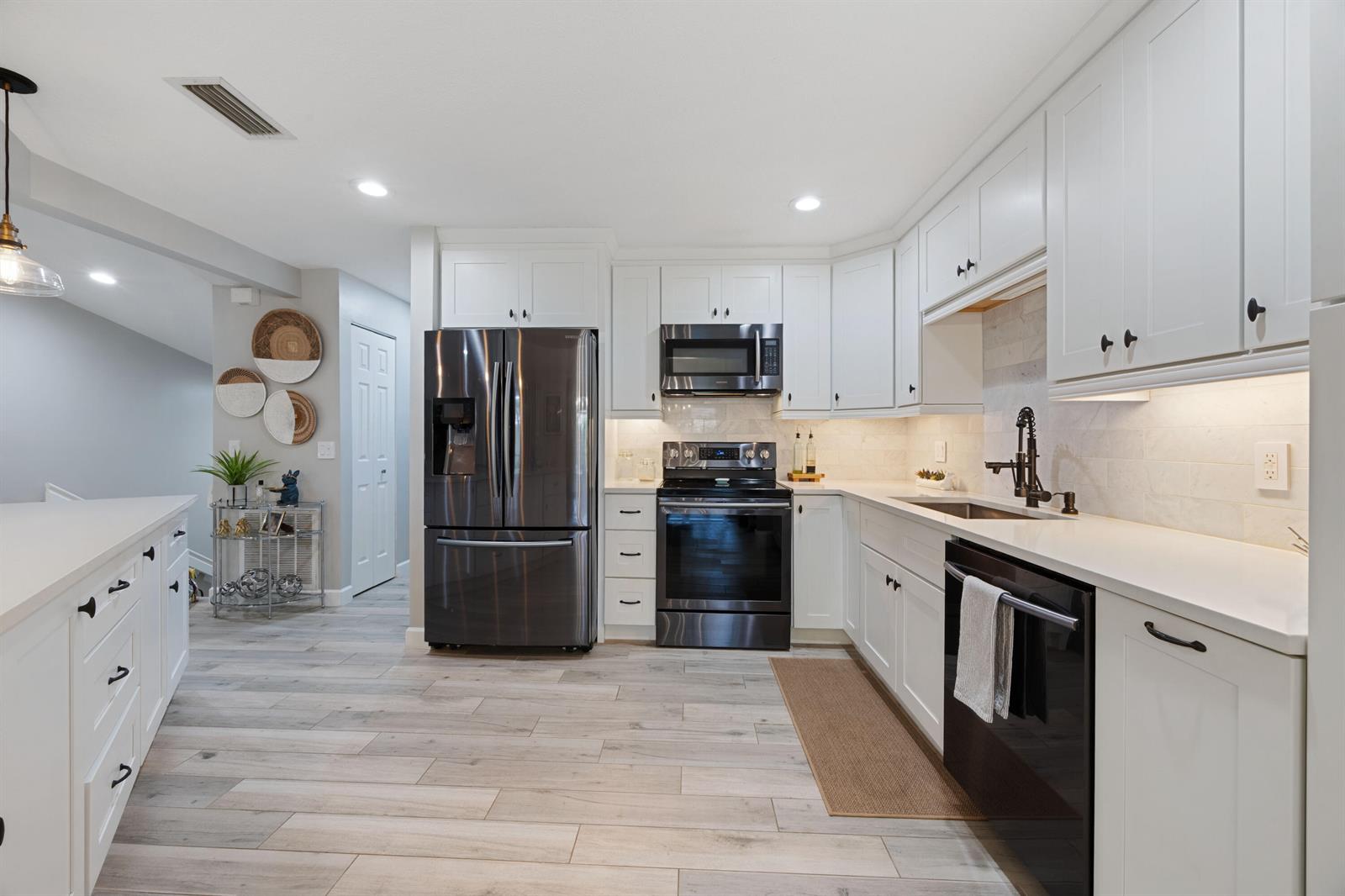A modern kitchen features white cabinets, stainless steel appliances, and light wood-look tile flooring — 5710 Coach House Circle # F, Boca Raton FL 33486, BOCA RATON, FL
