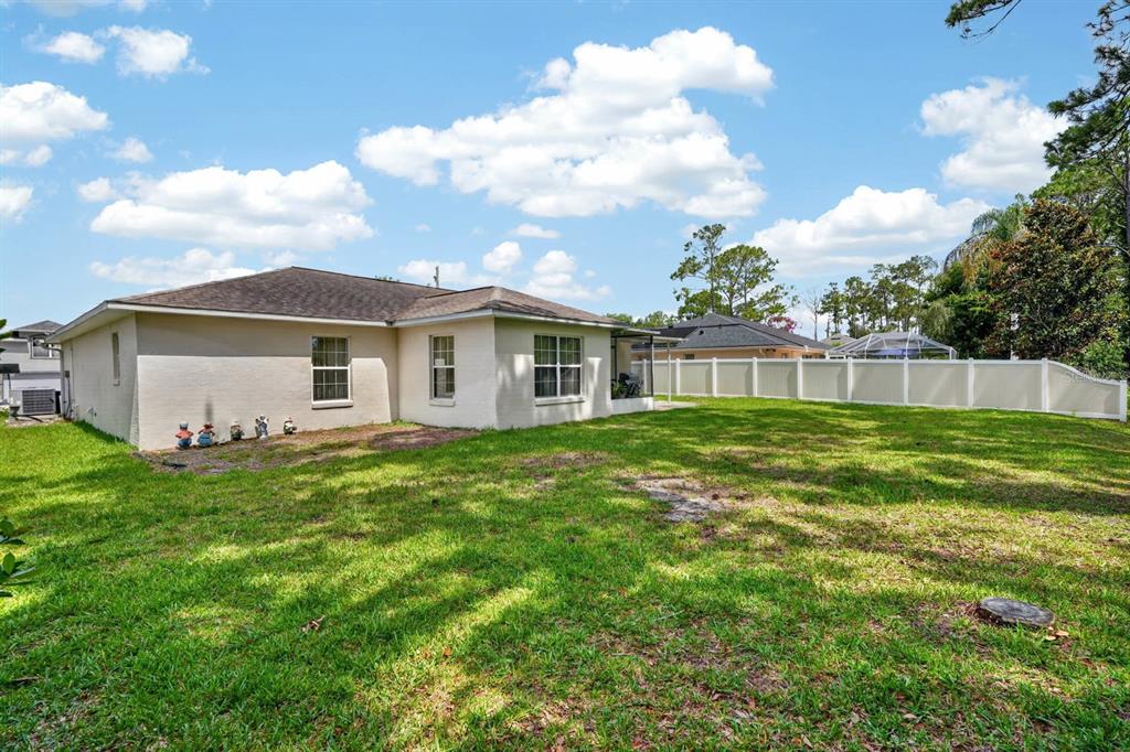 The exterior of a beige house features a large grassy backyard enclosed by a white fence — 80 ROXBORO, PALM COAST, FL