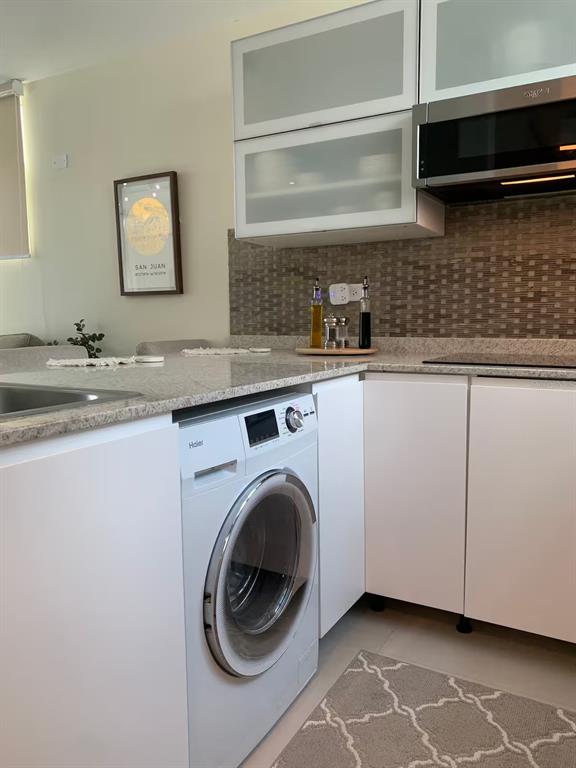 A kitchen features white cabinetry, a built-in washing machine, granite countertops, and a tiled backsplash — 1300 ASHFORD AVENUE UNIT 3A, SAN JUAN, PR
