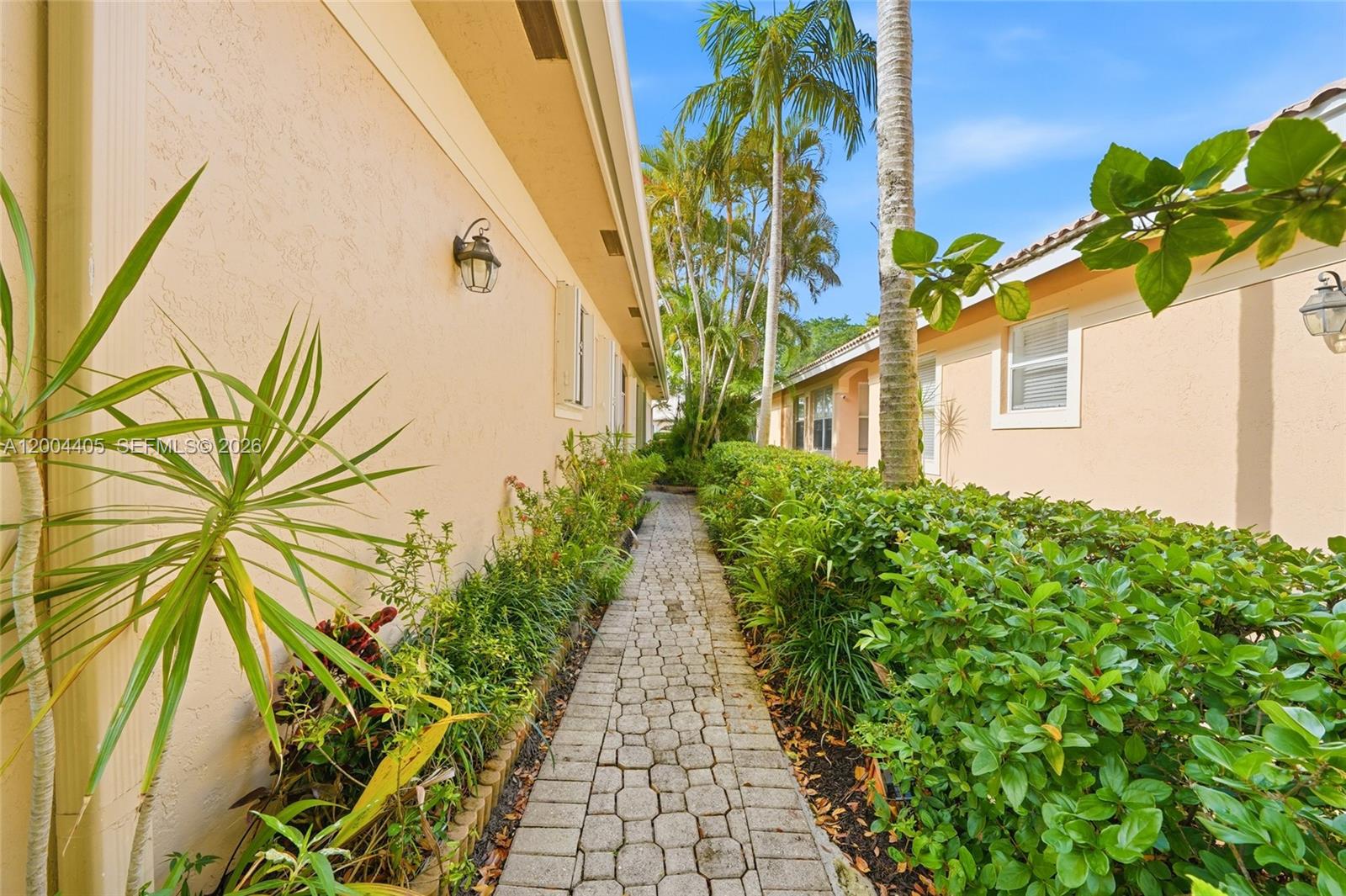 A stone walkway leads between two peach-colored stucco buildings lined with lush green landscaping — 2513 Coral Trace Pl # 0, Delray Beach FL 33445, DELRAY BEACH, FL