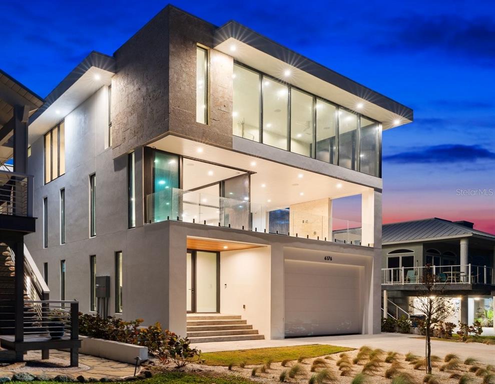 A modern three-story house with a garage, glass balconies, and large windows at dusk — 6176 S ATLANTIC AVENUE, NEW SMYRNA BEACH, FL