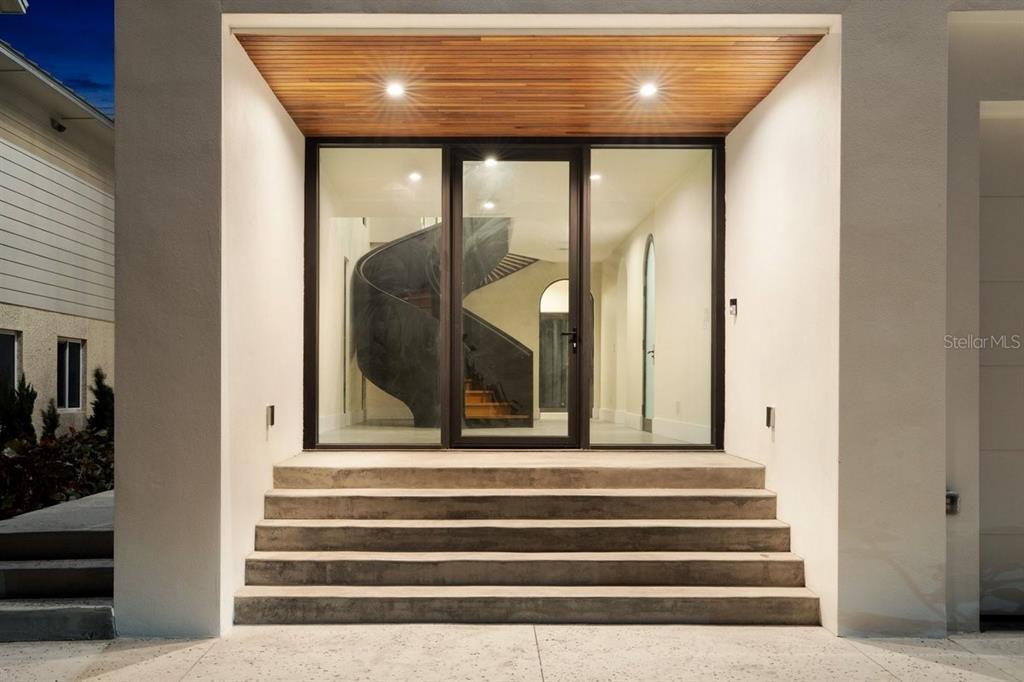 A modern entryway features concrete steps leading to a glass door with a spiral staircase inside — 6176 S ATLANTIC AVENUE, NEW SMYRNA BEACH, FL