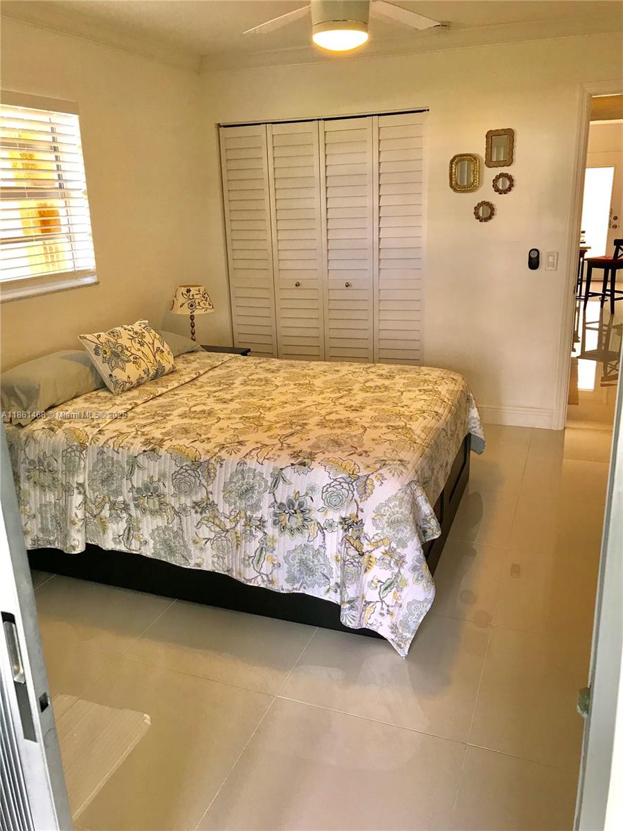 A bedroom features a bed with a floral quilt, white louvered closet doors, and tile flooring — 466 Normandy J # 466, Delray Beach FL 33484, DELRAY BEACH, FL