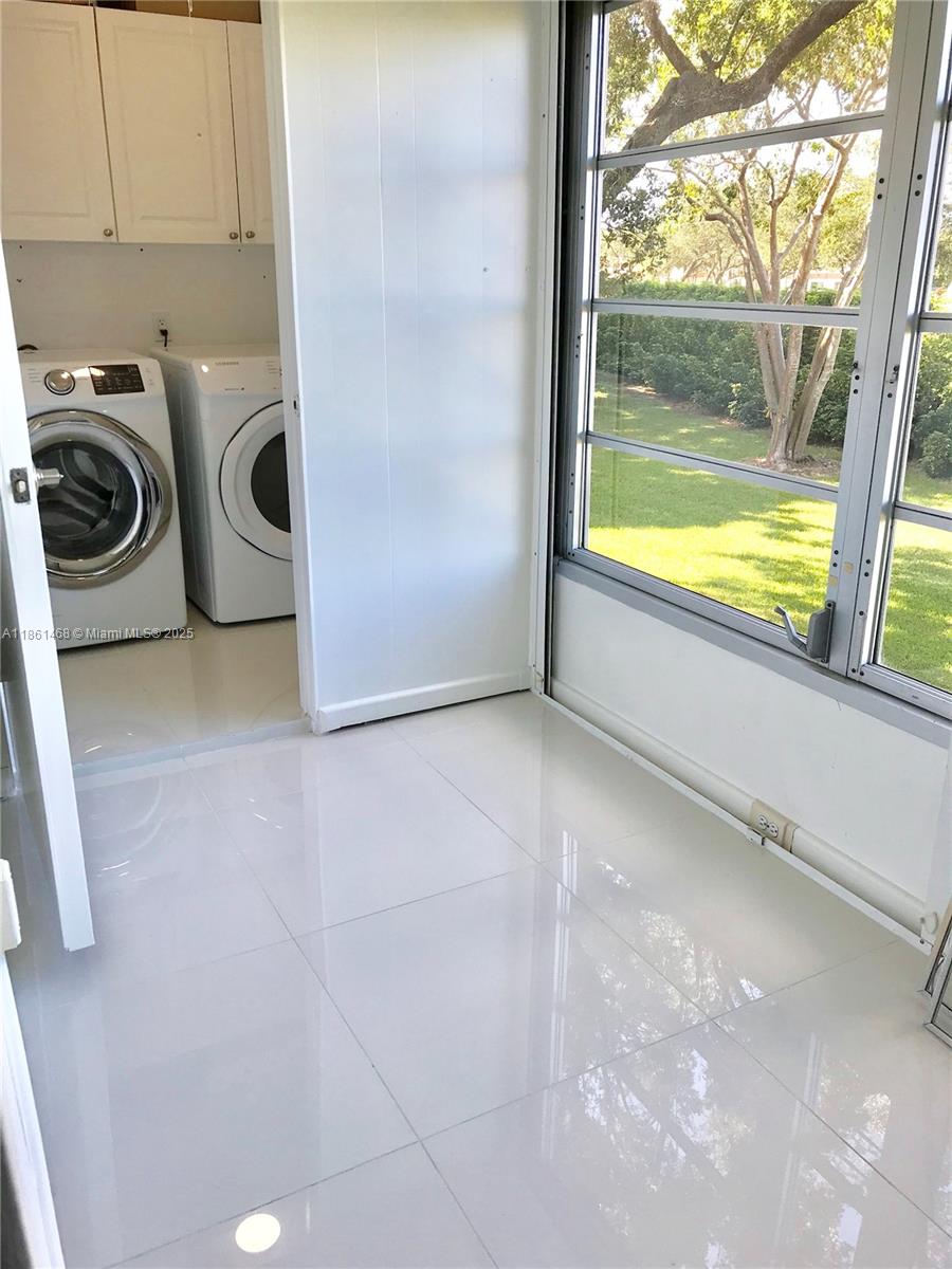 A laundry area with white appliances and cabinets sits next to a windowed sunroom — 466 Normandy J # 466, Delray Beach FL 33484, DELRAY BEACH, FL