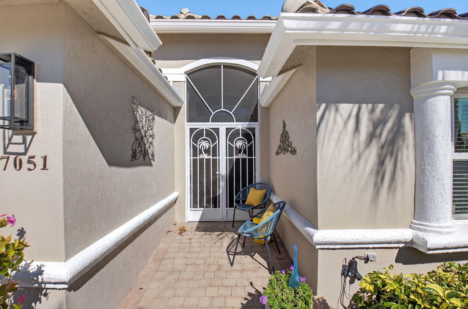 A paved entryway features a white decorative screen door, two blue chairs, and stucco walls — 7051 Trentino Way, Boynton Beach FL 33472, BOYNTON BEACH, FL
