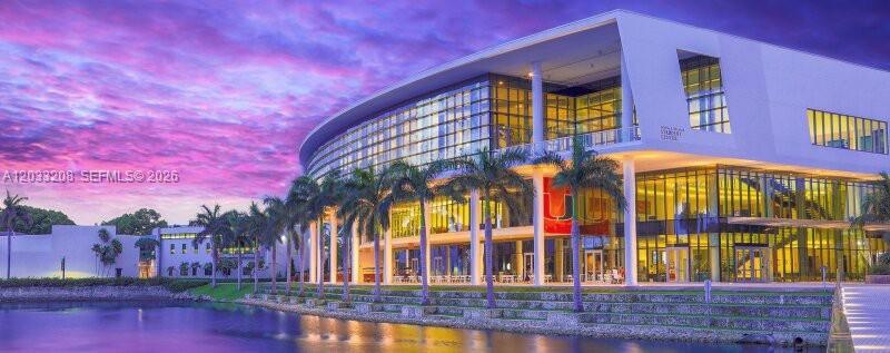 A modern building with glass walls and palm trees sits beside a lake at sunset — 9059 SW 73rd Ct, Miami FL 33156, MIAMI, FL