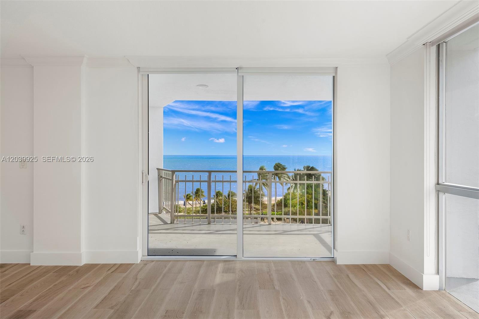 An empty room with light wood flooring features a sliding glass door opening to a balcony — 600 Grapetree Dr, Key Biscayne FL 33149, KEY BISCAYNE, FL
