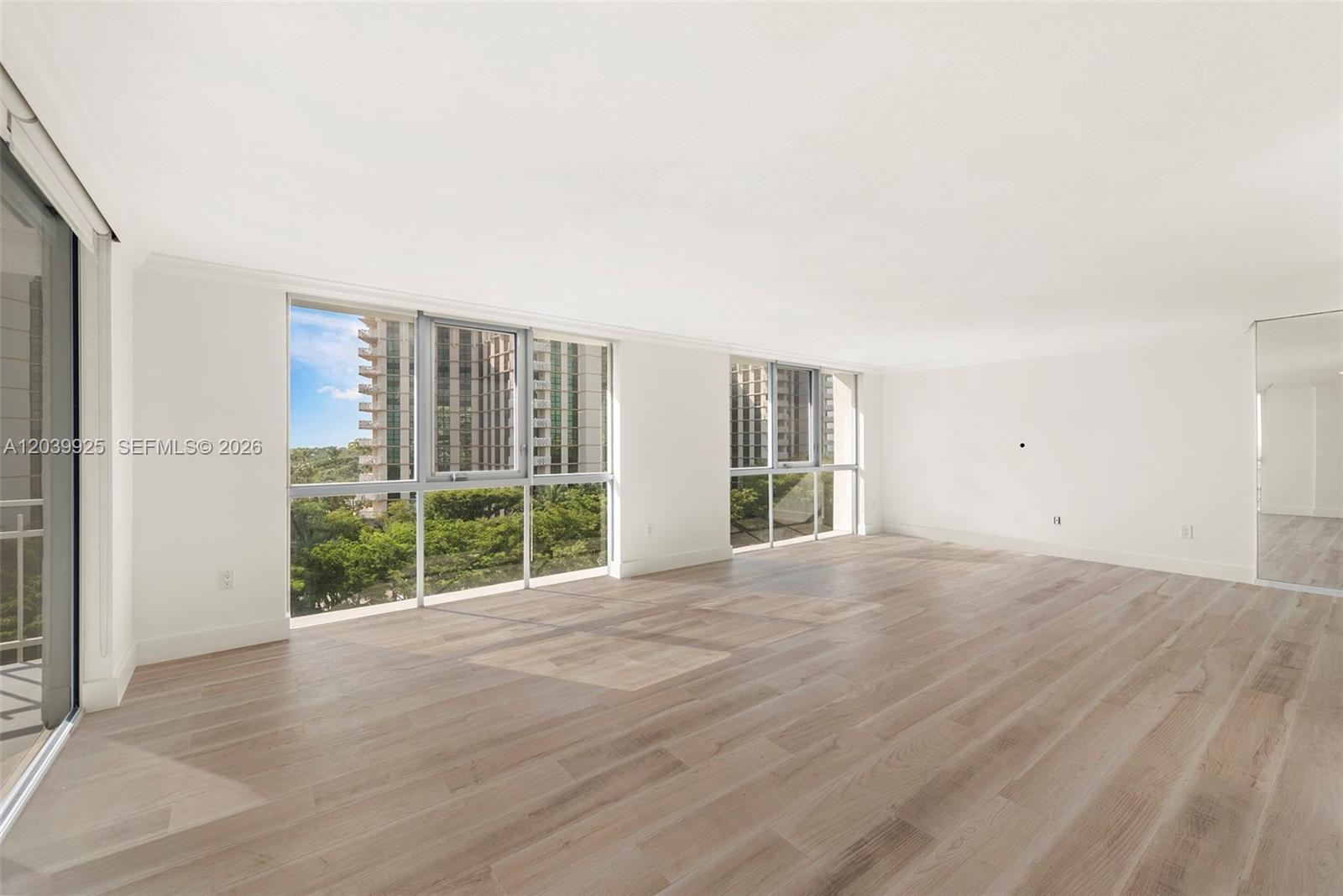 An empty room features light wood flooring, white walls, and large windows overlooking trees — 600 Grapetree Dr, Key Biscayne FL 33149, KEY BISCAYNE, FL
