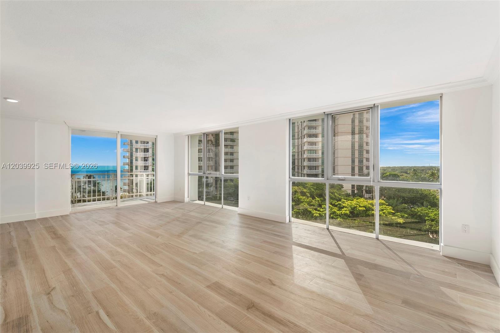 An empty room features light wood-look flooring, white walls, and large windows with ocean views — 600 Grapetree Dr, Key Biscayne FL 33149, KEY BISCAYNE, FL