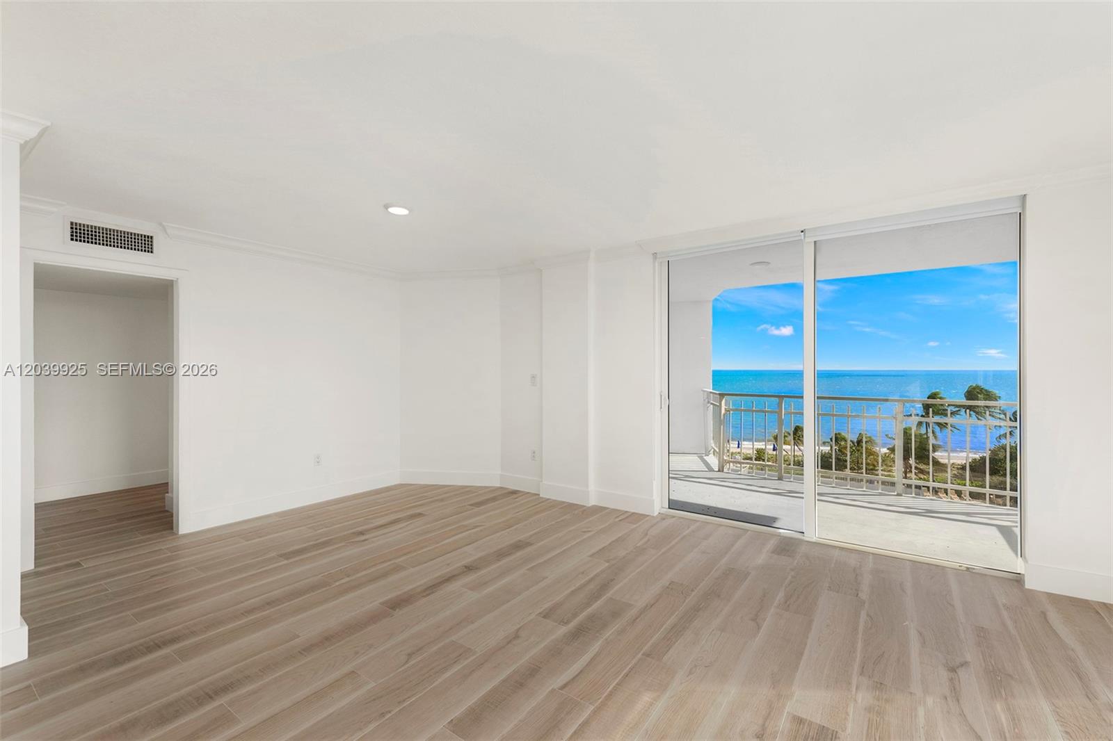 An empty room with light wood-look flooring features a sliding glass door to a balcony — 600 Grapetree Dr, Key Biscayne FL 33149, KEY BISCAYNE, FL